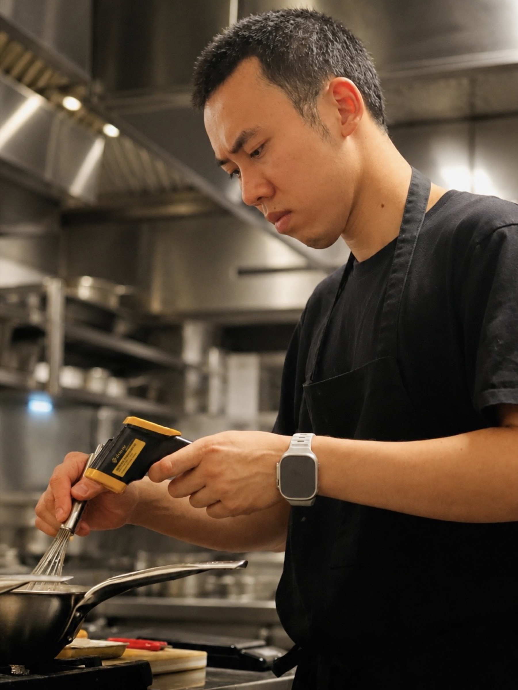 Chef Desmond Ho checking temperature with a probe thermometer while whisking a pan