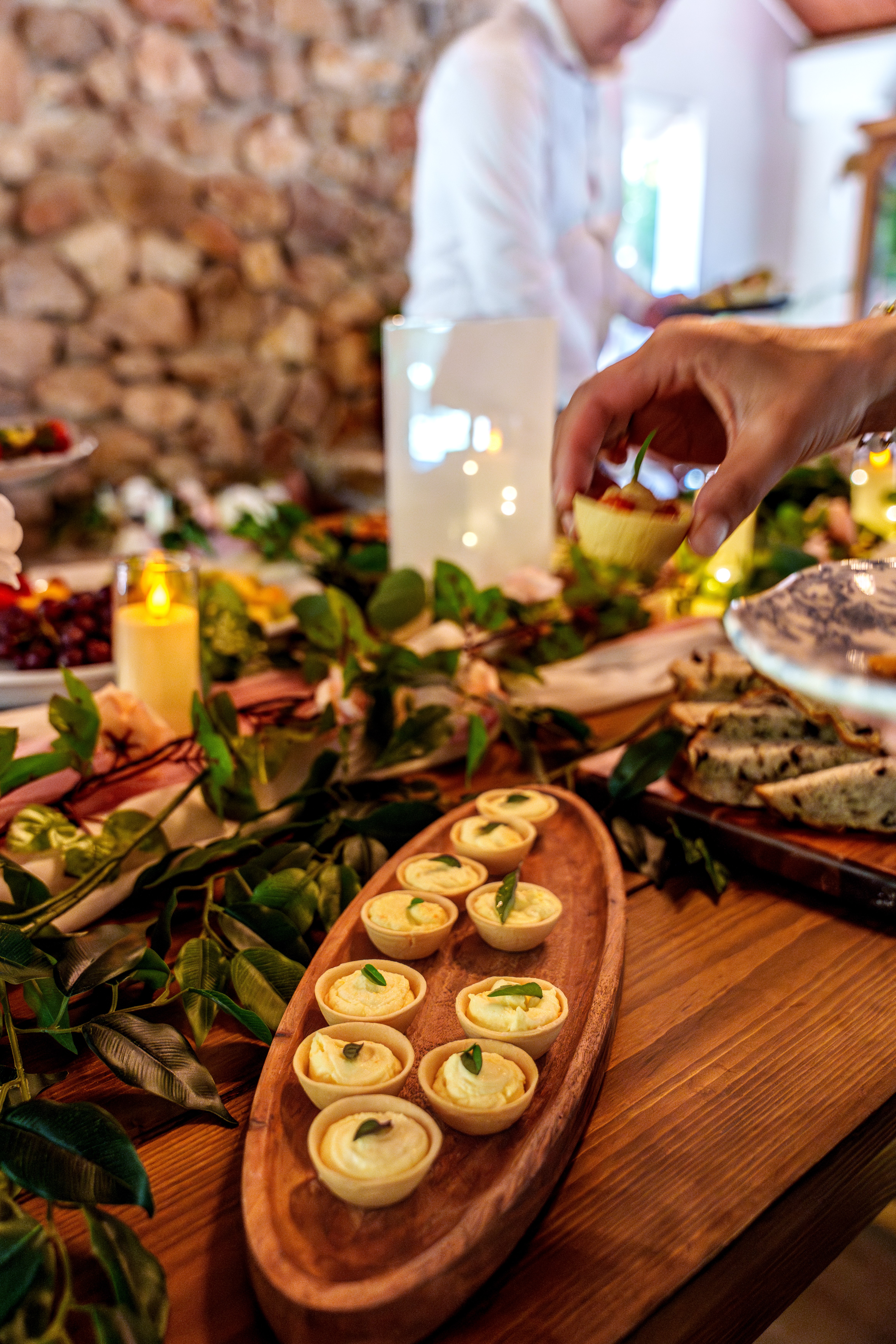 A guest reaching for a canapé from a wooden board of tartlets at a private event