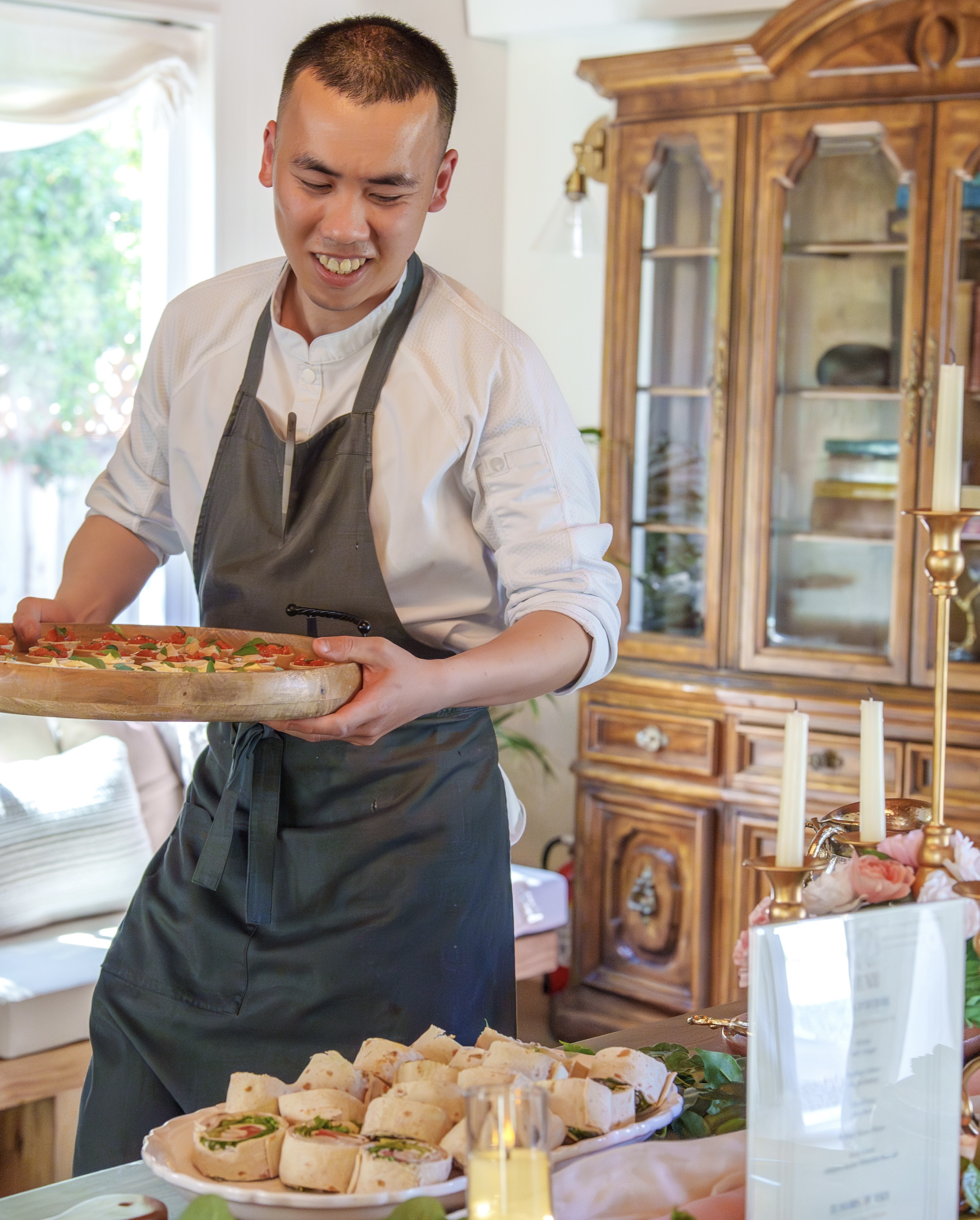 Chef Desmond Ho presenting a flatbread board over a table of canapés and sandwiches