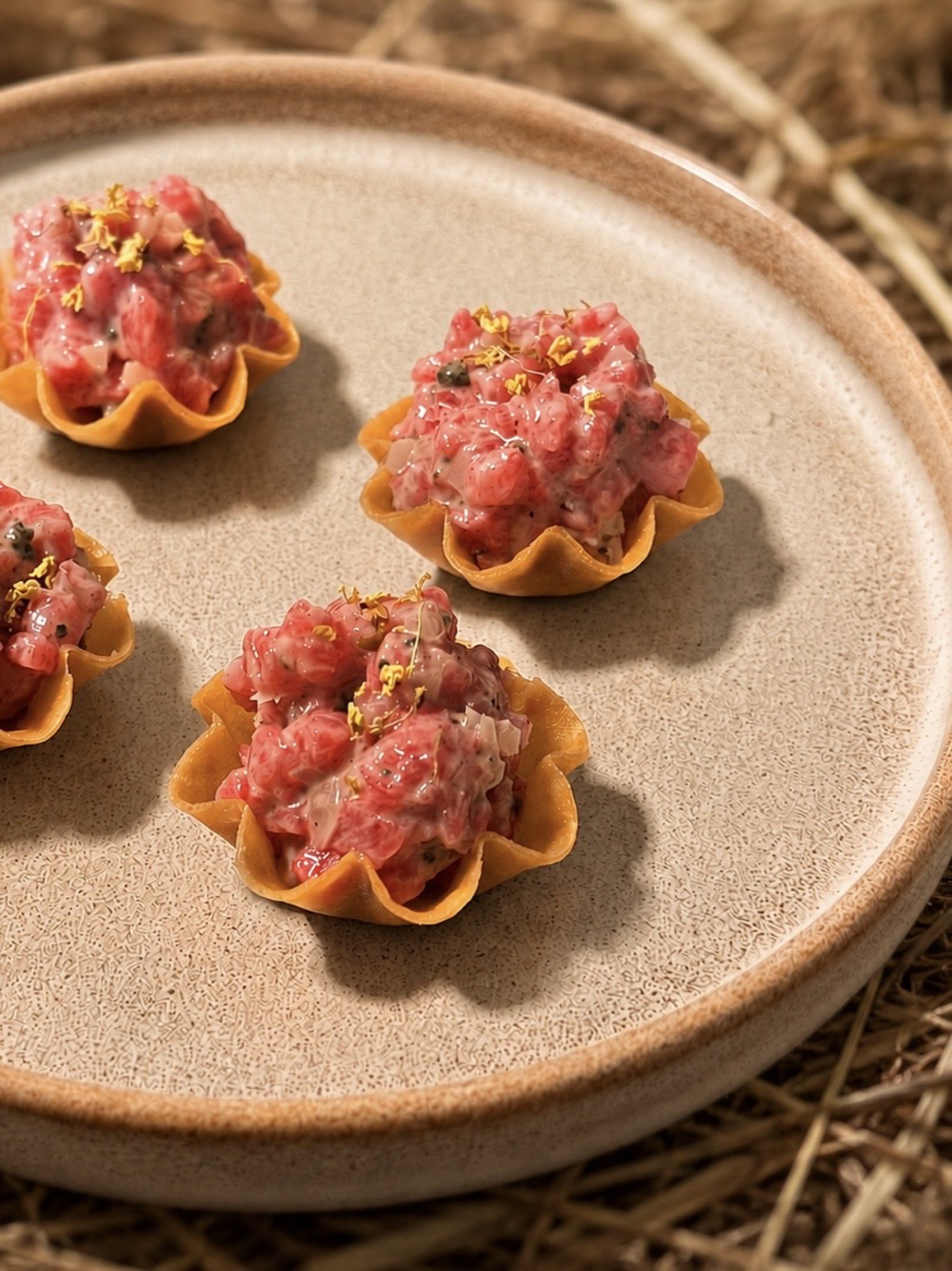 Beef tartare in crisp wonton cups, garnished and plated on a straw backdrop