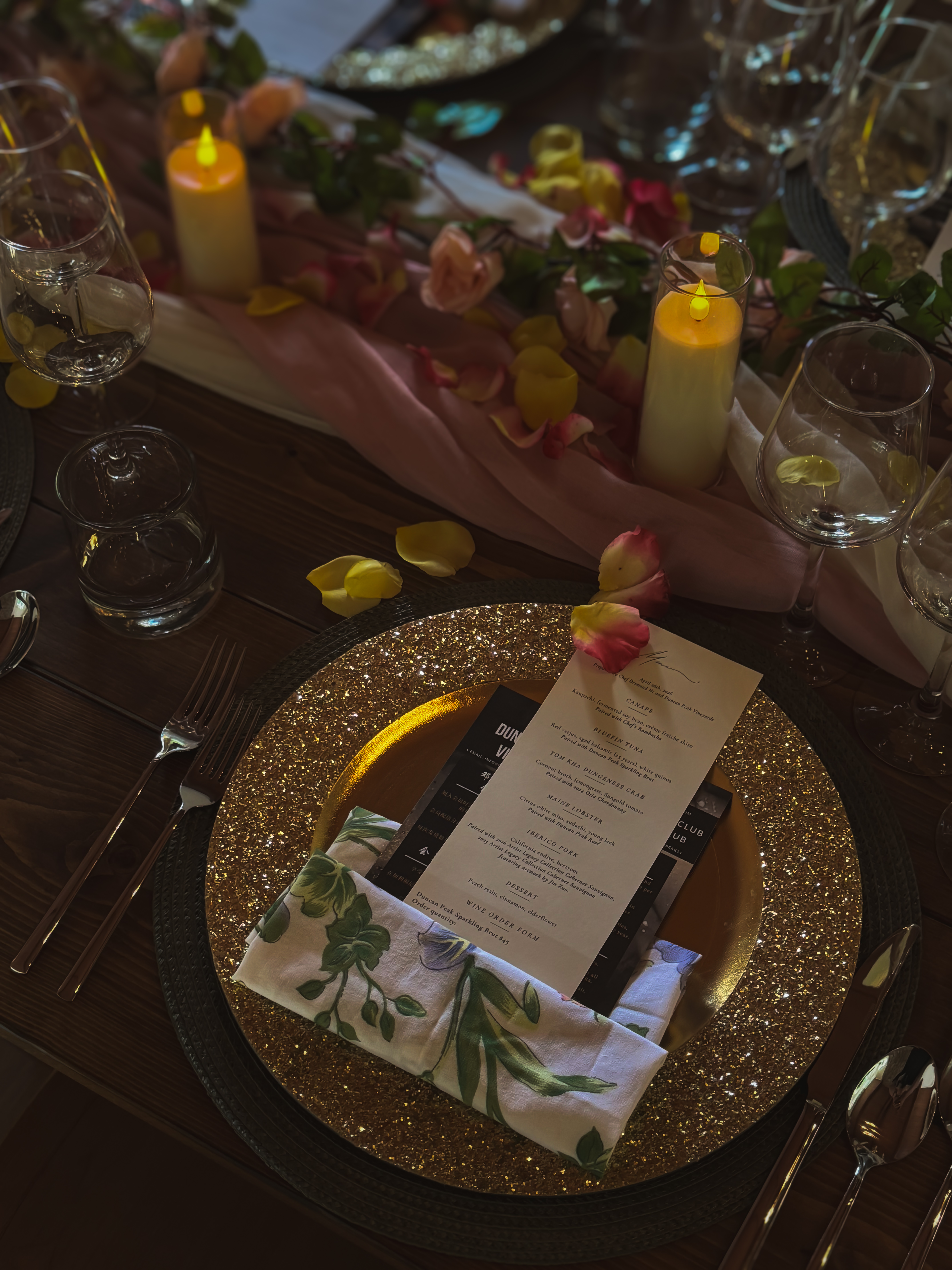 Printed menu card resting on a gold charger between candles and rose petals