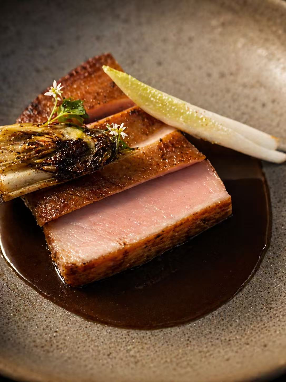 A close-up of a pink-roasted duck breast on a textured ceramic plate