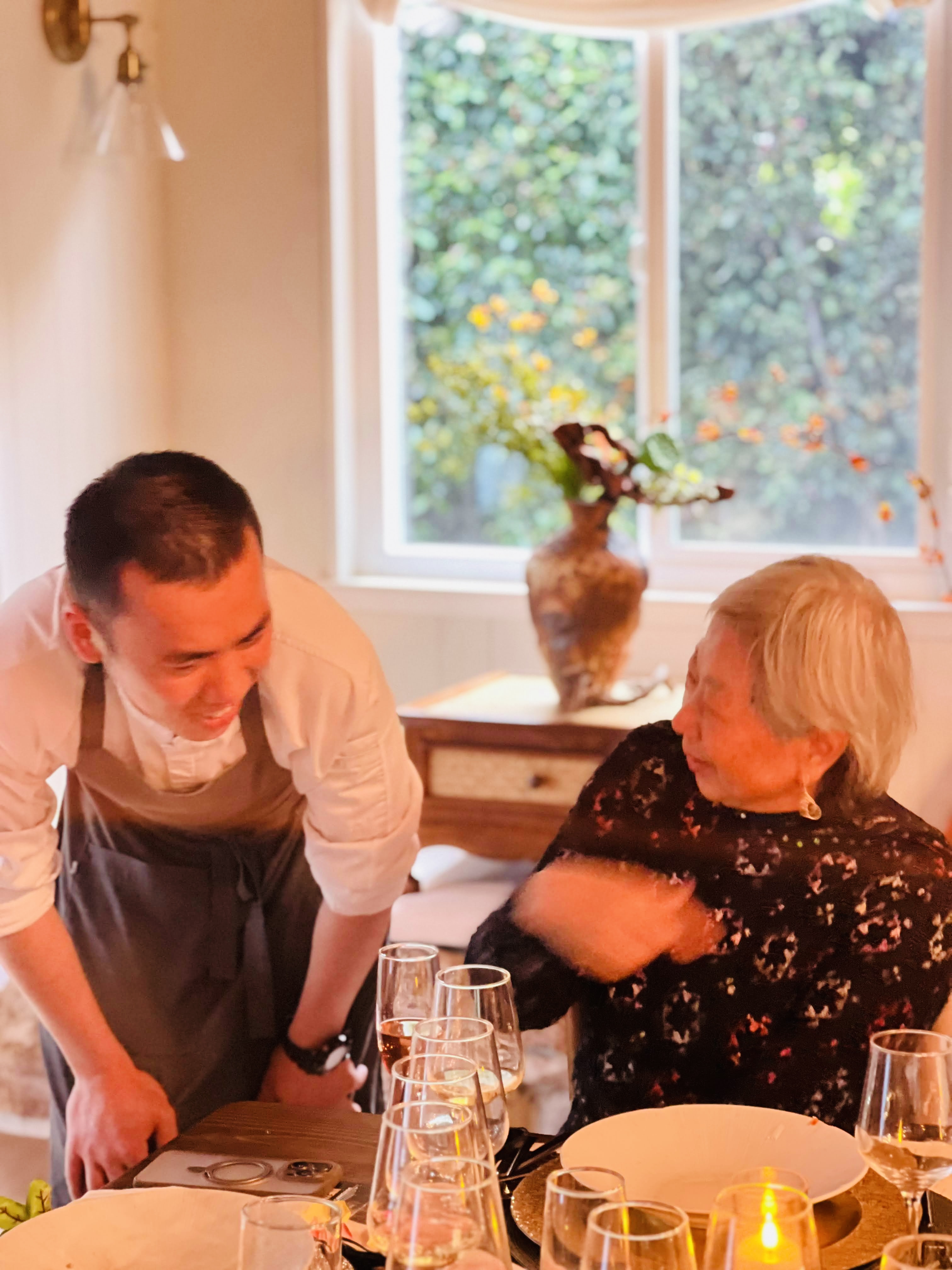 Chef Desmond presenting a course to a seated guest by the window
