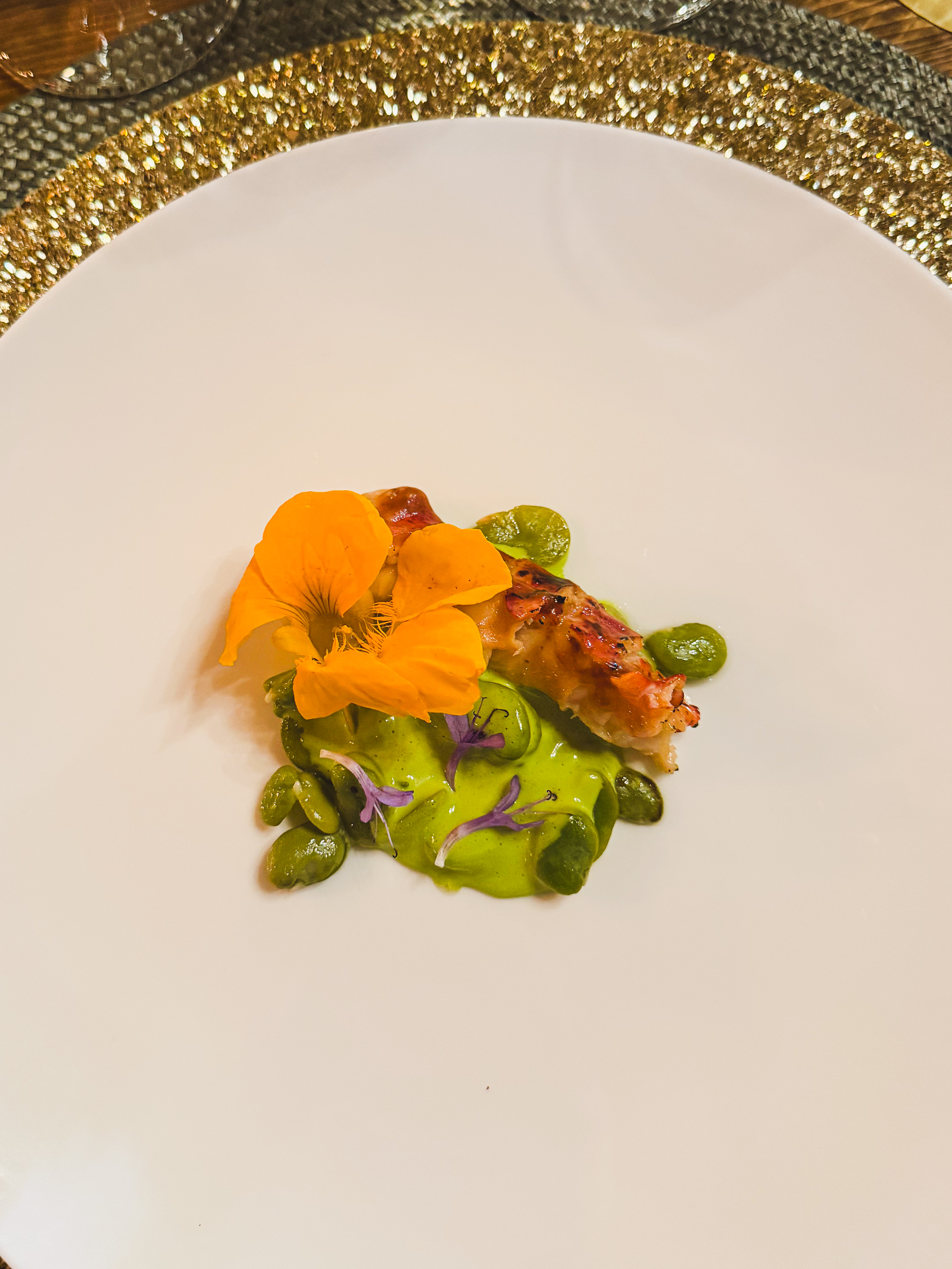 A small plated course with an edible orange flower and green sauce