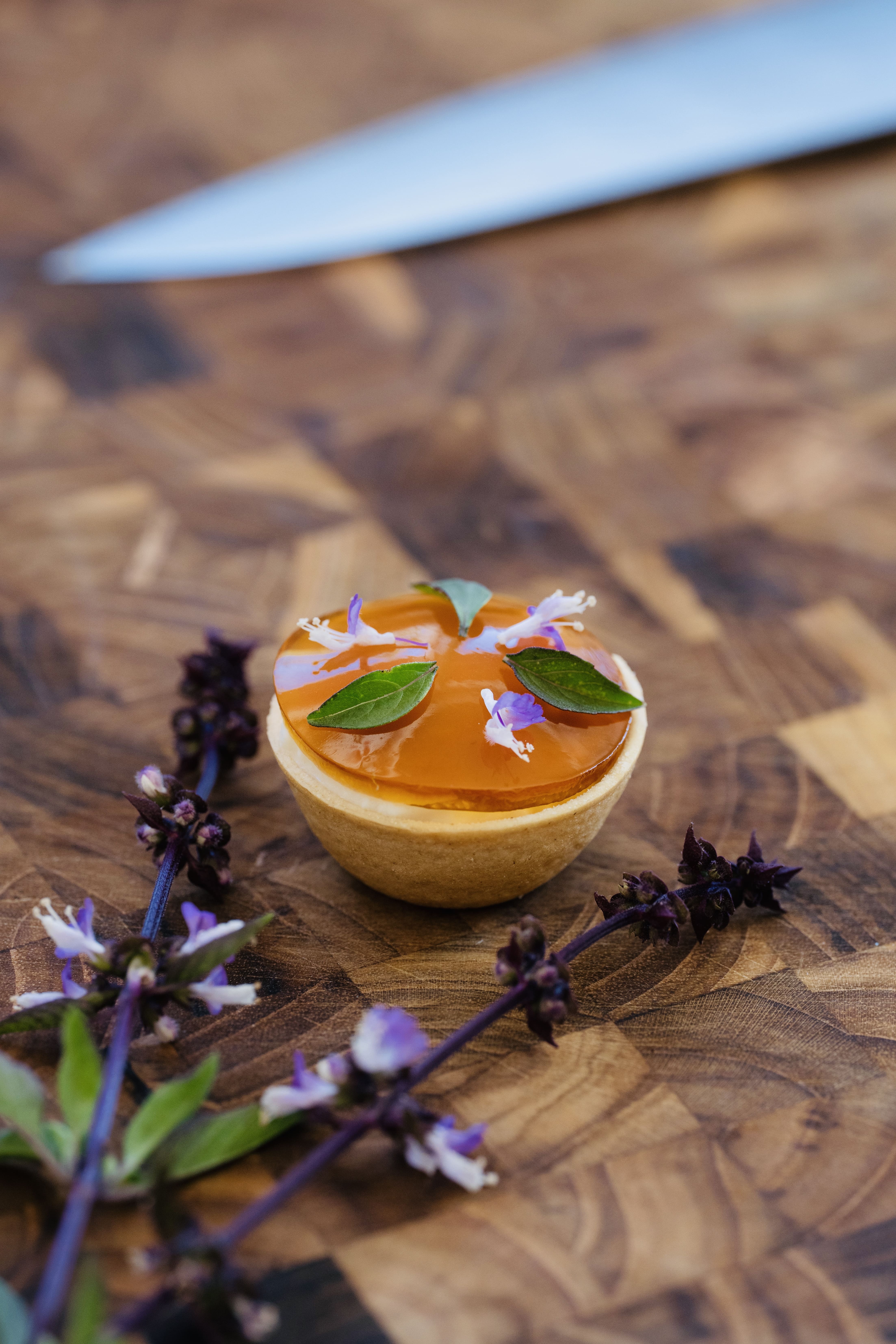 A small apricot-glazed tartlet garnished with edible flowers on a wooden board