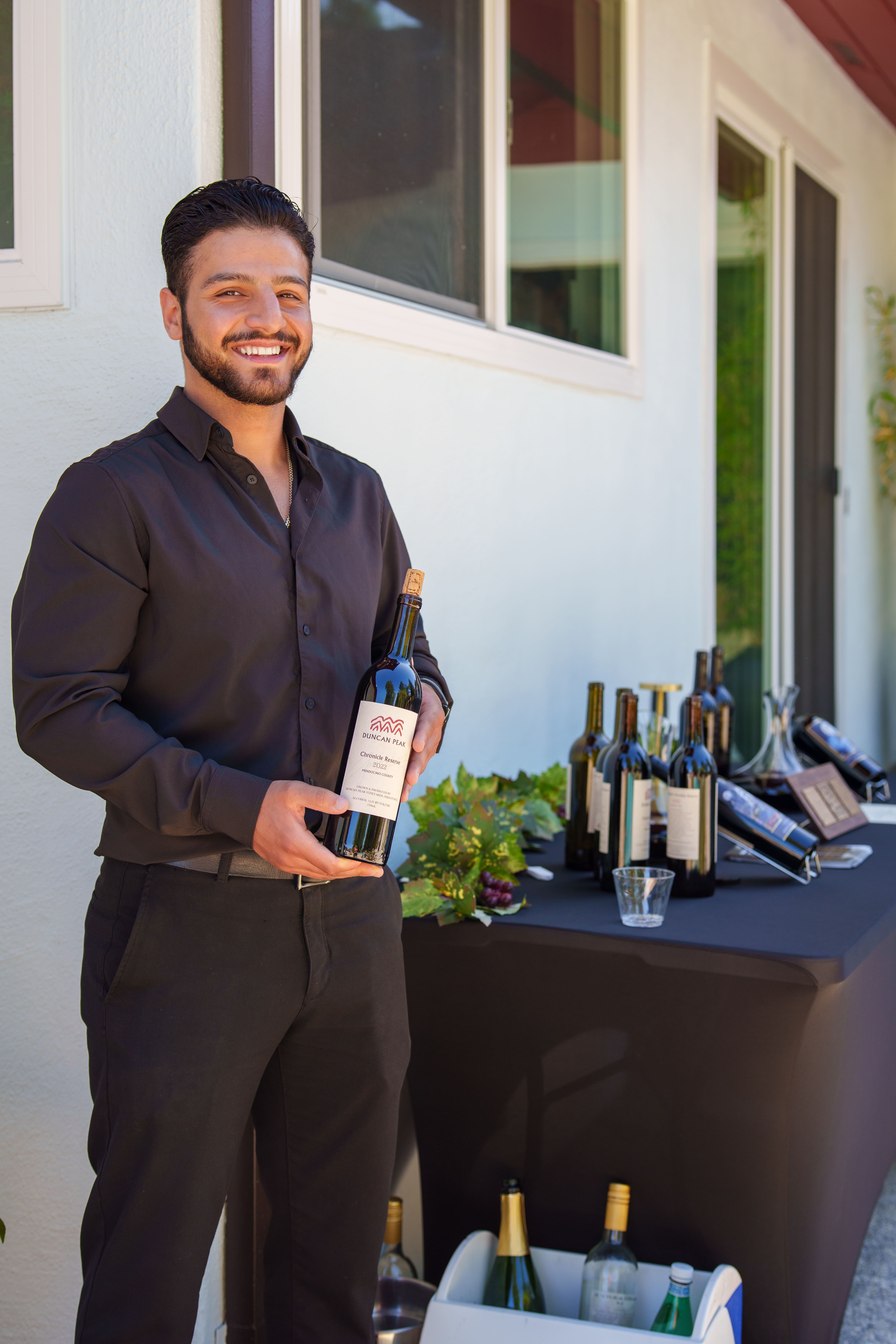 A sommelier in dark shirt presenting a bottle of Duncan Peak Chronicle Reserve