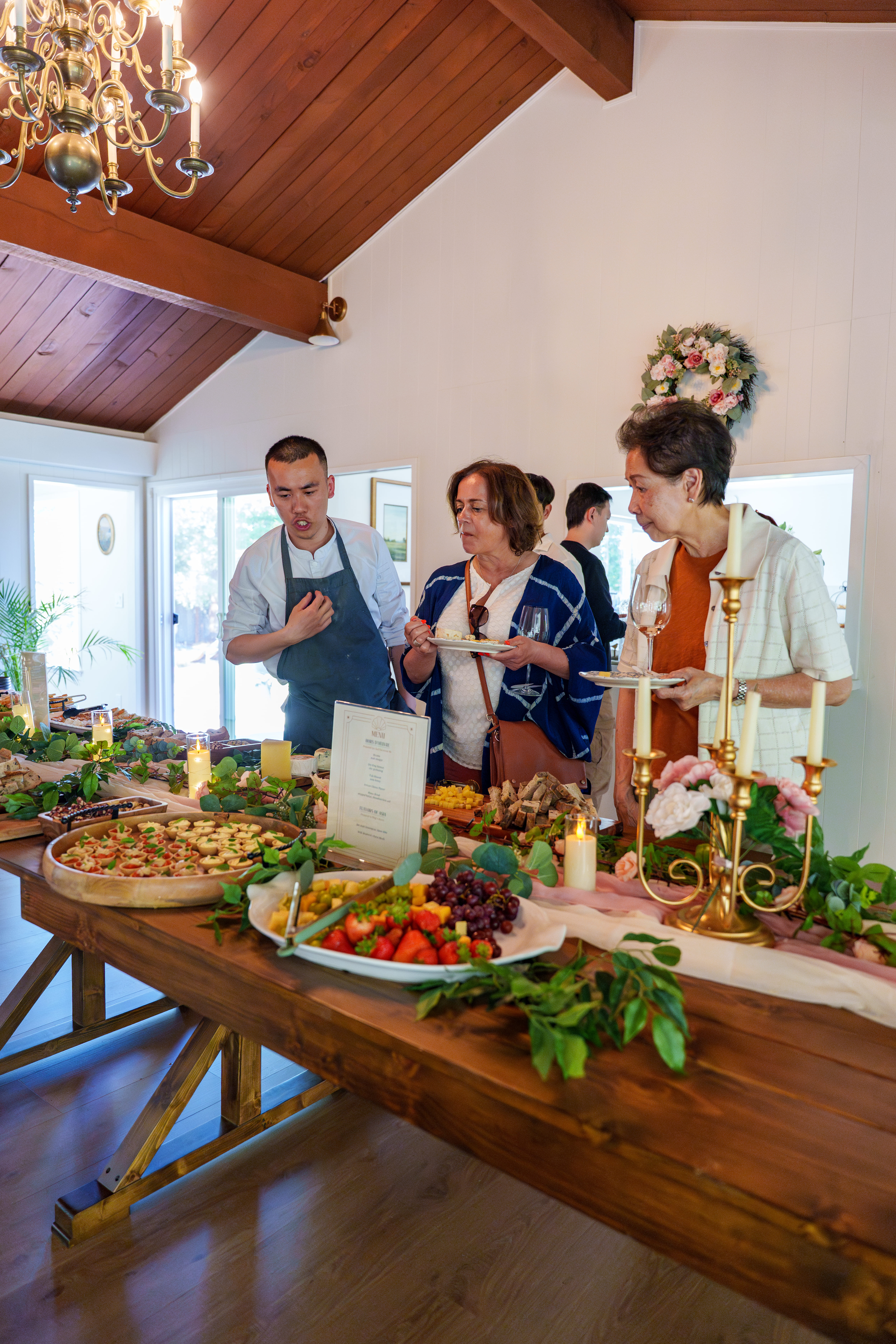 Chef Desmond explaining a dish to two seated guests at the grazing table