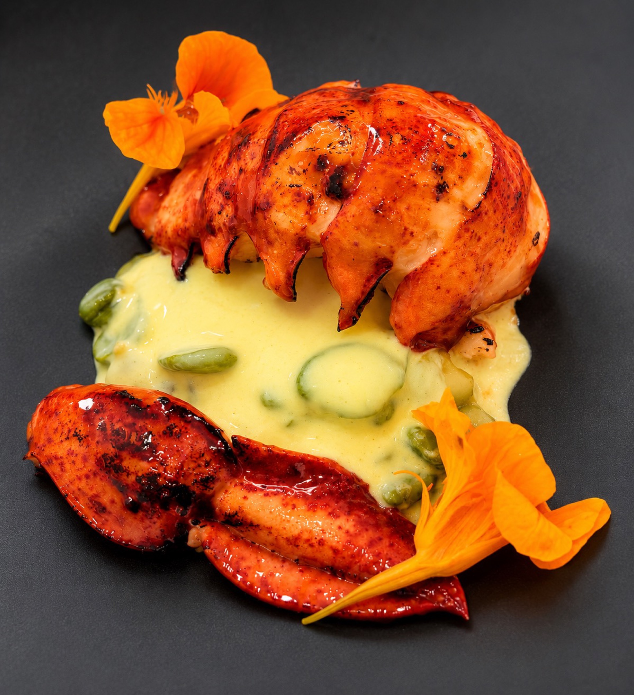 Charred lobster and crab claws over a beurre blanc with fava beans and nasturtium flowers